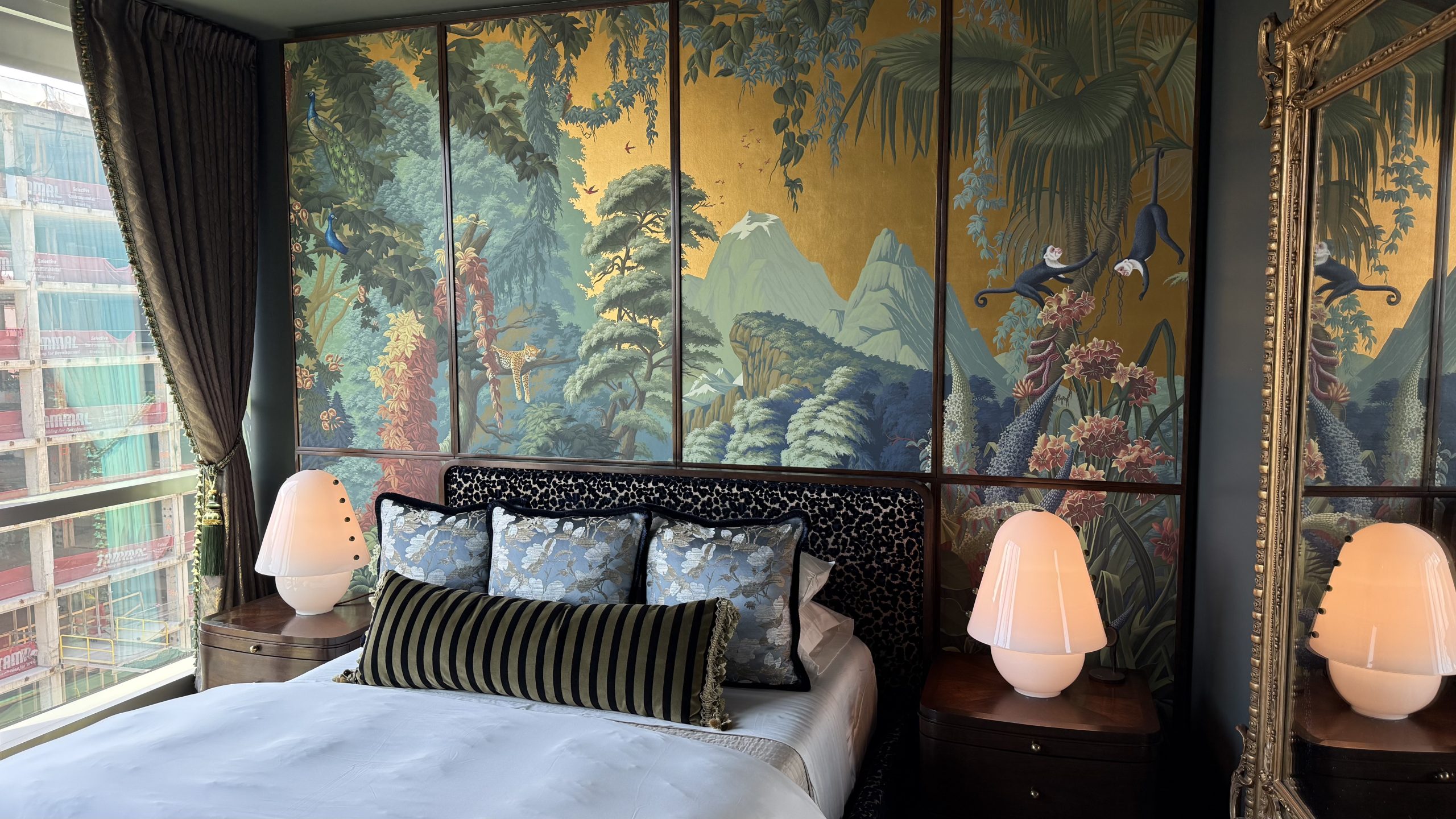 Custom bed beneath hand-painted landscape panels, with pink lamps and a gilded mirror